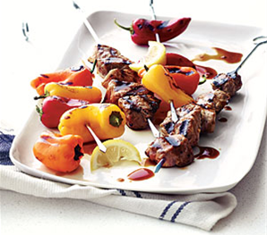 Kebab skewers with pork, mini red, yellow,
and orange bell peppers with onions,
sauce, and a lemon wedge garnish.