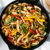 Cast-iron skillet of sliced chicken strips, red and green bell peppers, and onions