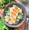 Bowl with a bed of cubed potato salad tossed with green beans and a sliced grilled chicken breast on top