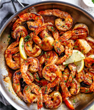 Metal skillet with shrimp tossed in a honey garlic sauce and lemon wedges nestled throughout