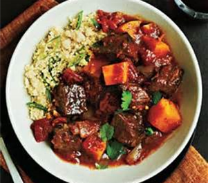 A white bowl of stewed beef and butternut squash over a bed of couscous