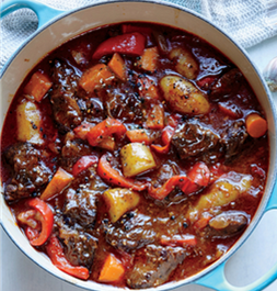 Soup pot filled with simmered beef cubes, potatoes, carrots, red bell pepper, onion, and celery

