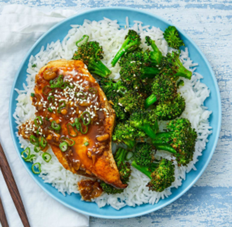 Plated meal of jasmine rice, steamed broccoli, honey sesame chicken breast, garnished with sesame seeds and green onions

