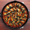 Cast-iron skillet of sliced tomato, squash, zucchini, eggplant, layered in spiral pattern with red sauce and fresh herbs