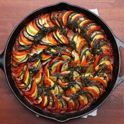 Cast-iron skillet of sliced tomato, squash, zucchini, eggplant, layered in spiral pattern with red sauce and fresh herbs