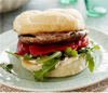 Portobello mushroom burger with sliced roasted red peppers, arugula and creamy sauce between a kaiser roll on a plate