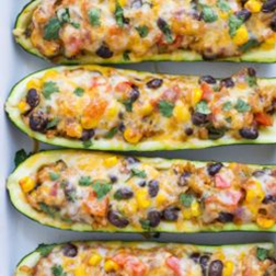 4 halved zucchinis stuffed with black beans, corn, red pepper, salsa, tomatoes topped with melted cheese on a sheet pan