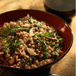  A brown bowl with barley risotto mixed with mushrooms and greens