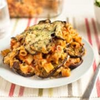 A white plate of baked eggplant topped with pasta, red sauce, and cheese